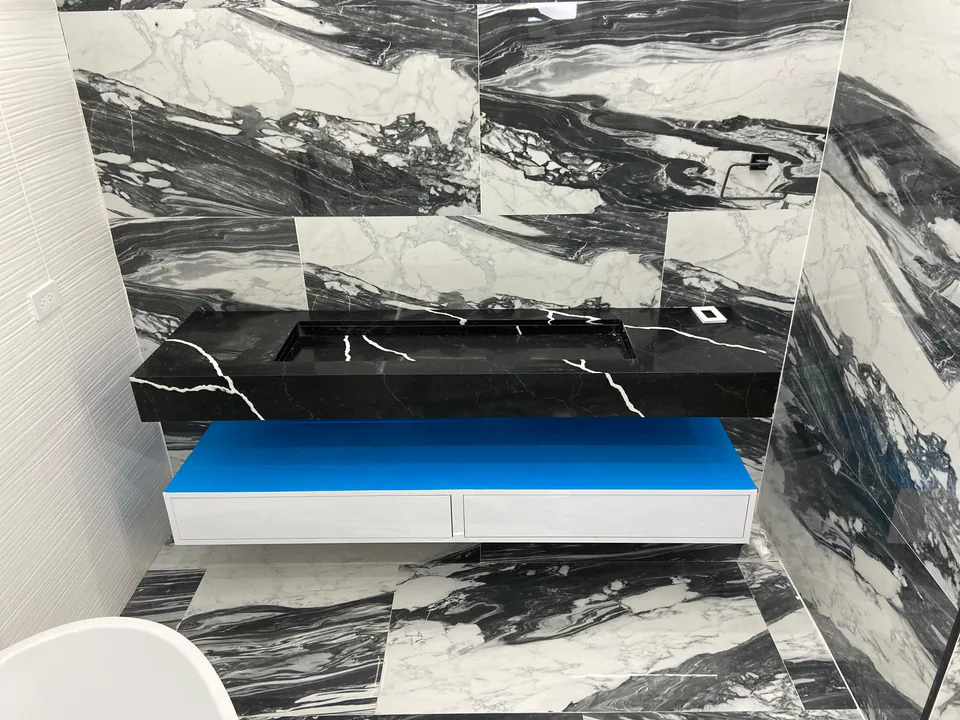 Baño trabajado por M5 con superficies marmoleadas en blanco y negro y mueble suspendido.